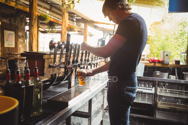 Bar tender filling beer from bar pump at bar counter — Stock Photo