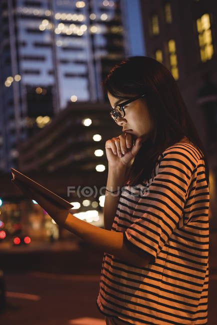 Nachdenkliche junge Frau nutzt nachts digitales Tablet auf der Straße — Stockfoto