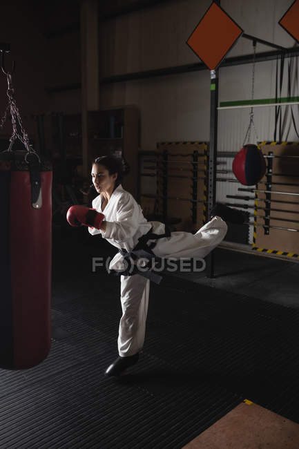 Sportlerin übt Karate mit Boxsack im dunklen Fitnessstudio — Stockfoto