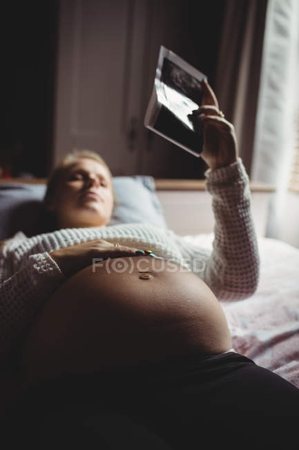Беременная женщина смотрит на ультразвук в спальне дома — стоковое фото