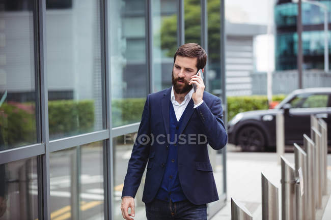 Businessman talking on mobile phone while walking on footpath — Stock Photo