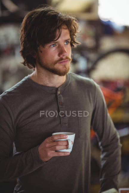 Удумливий чоловік має чашку кави в велосипедному магазині — стокове фото