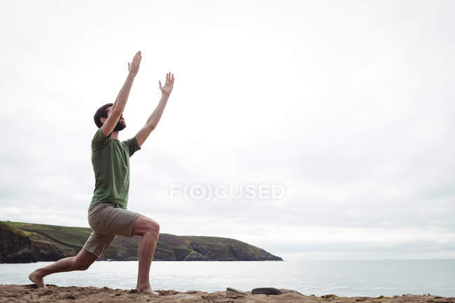 Человек, выполняющий упражнения на растяжку на пляже — стоковое фото