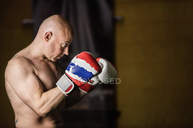 Vista laterale del boxer thailandese muscoloso senza camicia che pratica la boxe in palestra — Foto stock
