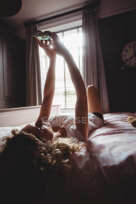 Belle femme prenant selfie sur téléphone portable dans la chambre à coucher à la maison — Photo de stock