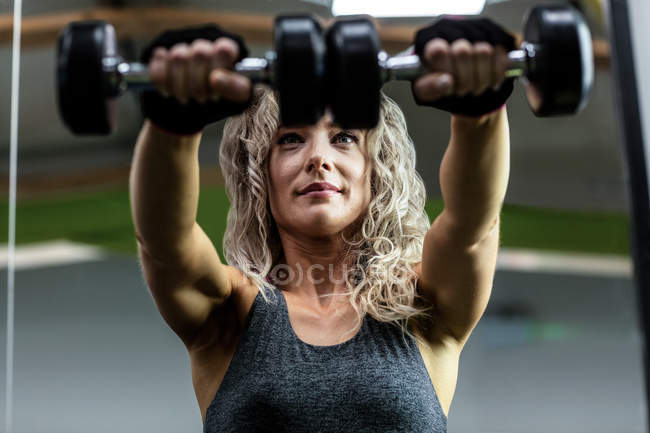 Красива жінка, що піднімає гантелі в спортзалі — стокове фото