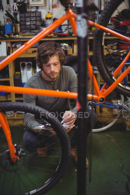 Mechanic writing on clipboard in bicycle shop — Stock Photo