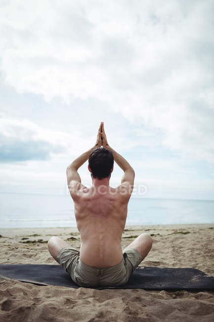 Вид сзади на человека, занимающегося йогой на пляже — стоковое фото