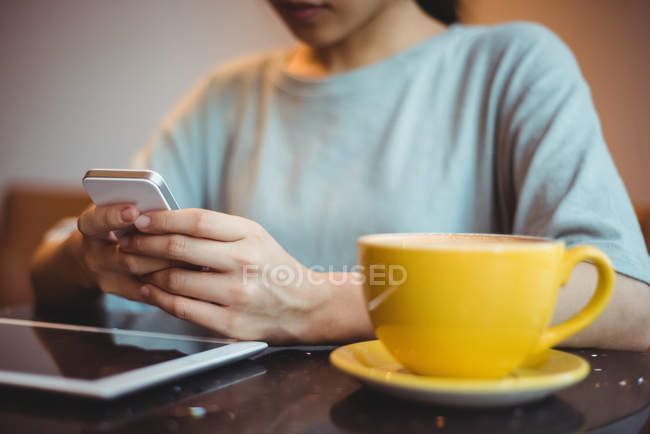 Donna che utilizza il telefono cellulare mentre prende un caffè al caffè — Foto stock