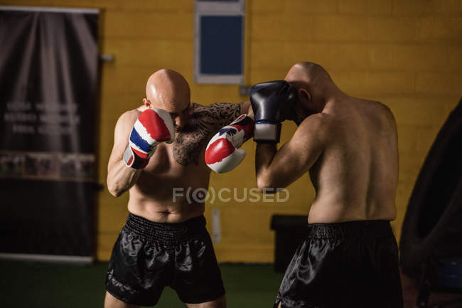 Vista lateral de dos boxeadores tailandeses sin camisa practicando en el gimnasio - foto de stock