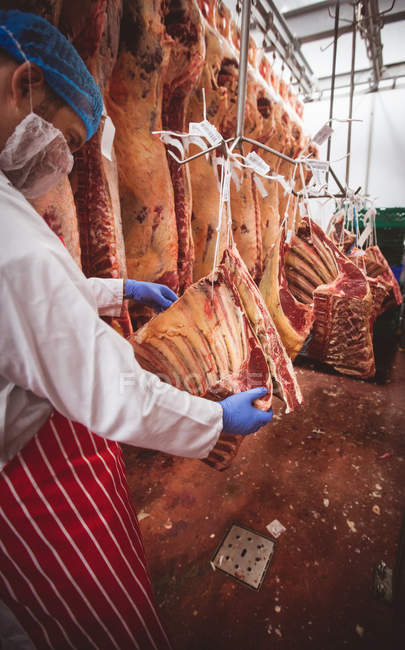 Carnicero colgando carne roja en el almacén de la carnicería - foto de stock