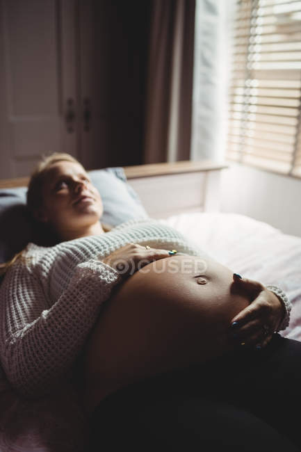 Задумчивая беременная женщина отдыхает в спальне дома — стоковое фото