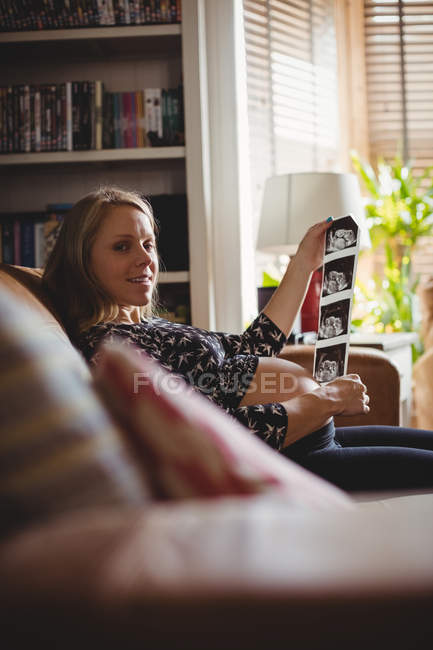 Portrait of pregnant woman holding sonography in living room at home — Stock Photo
