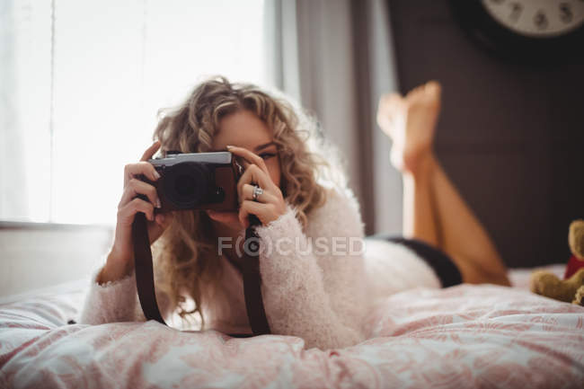 Mujer tomando fotos en cámara digital en el dormitorio en casa - foto de stock