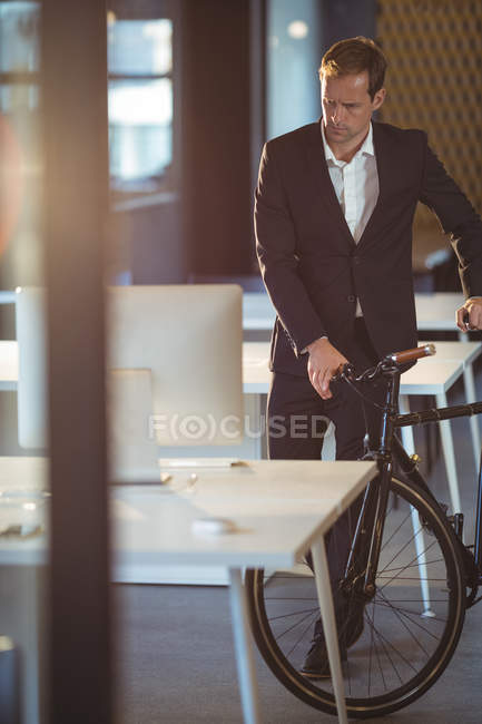 Бизнесмен, стоящий с велосипедом в офисе — стоковое фото
