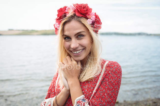 Heureuse femme blonde en fleur tiare regardant la caméra près de la rivière — Photo de stock