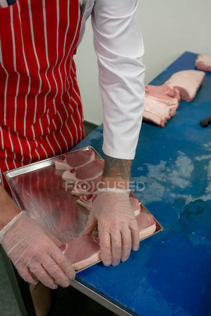 Mid section of butcher arranging steaks in tray at butchers shop — Stock Photo