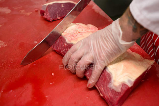 Hands of butcher slicing red meat at butchers shop — Stock Photo