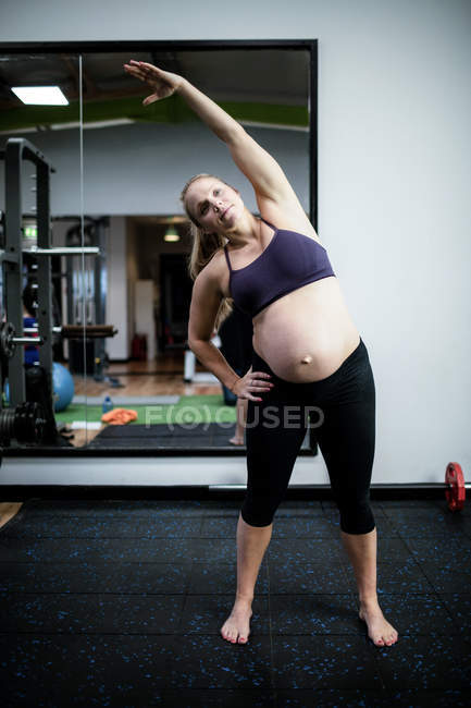 Беременная женщина выполняет упражнения на растяжку в тренажерном зале — стоковое фото