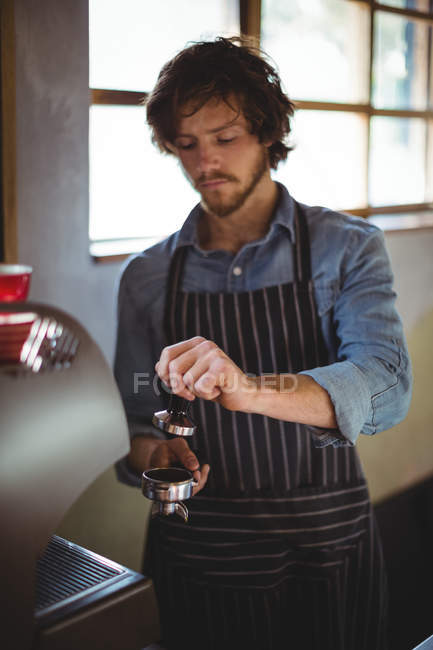 Waiter using a tamper to press ground coffee into a portafilter in cafe at workshop — Stock Photo