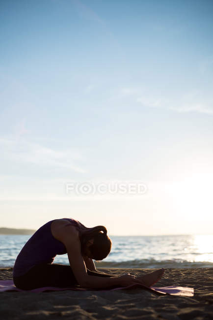 Vista lateral da mulher praticando ioga na praia no dia ensolarado — Fotografia de Stock