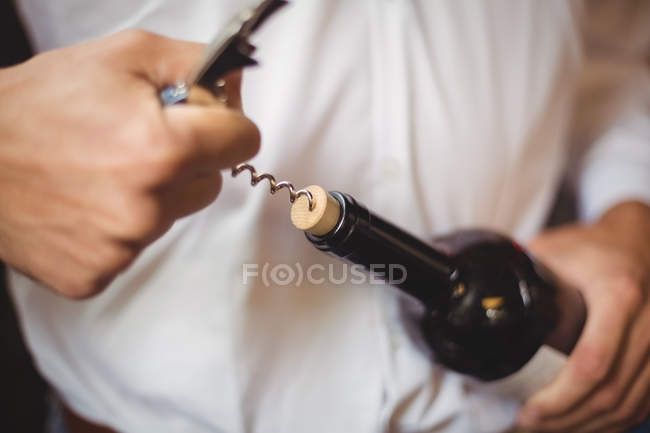 Mid section of bar tender opening a bottle of wine at bar counter — Stock Photo
