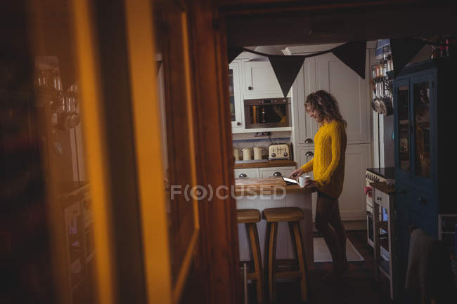 Frau nutzt digitales Tablet beim Kaffee in der heimischen Küche — Stockfoto