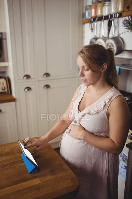 Schwangere nutzt digitales Tablet zu Hause in der Küche — Stockfoto