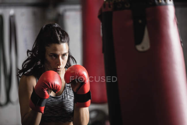 Ritratto di pugile donna che pratica pugilato con sacco da boxe in palestra — Foto stock