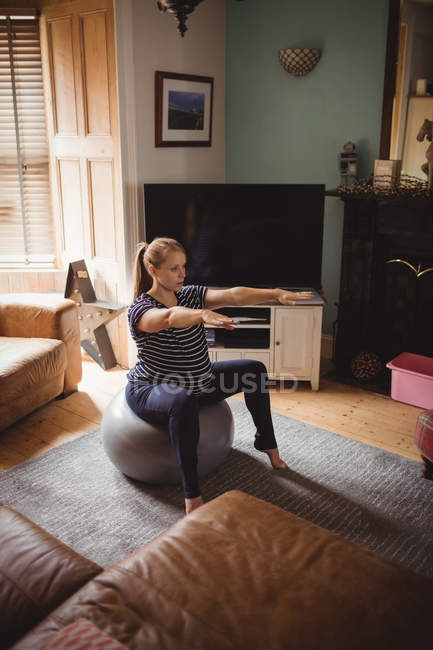 Высокий угол зрения беременной женщины, выполняющей упражнения на растяжку на фитнес-мяч в гостиной на дому — стоковое фото