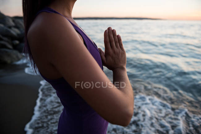 Sección media de la mujer meditando en la playa en el día soleado - foto de stock