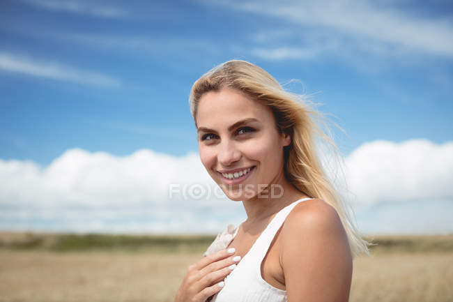 Sorrindo mulher atraente em pé no campo e olhando para a câmera — Fotografia de Stock
