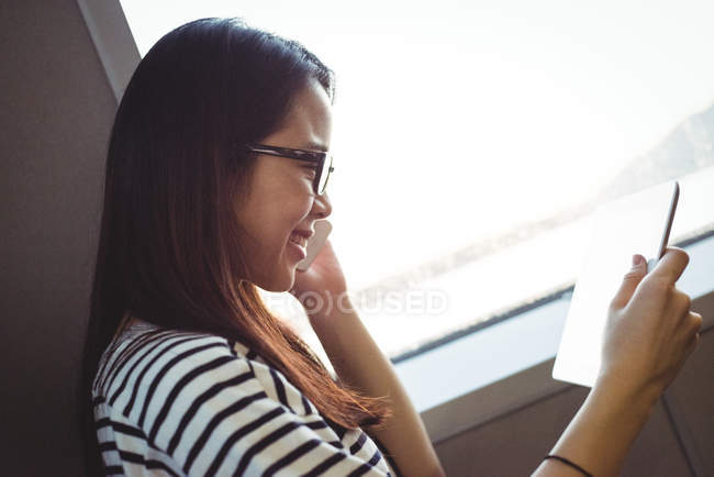 Young woman talking on mobile phone while using digital tablet — Stock Photo