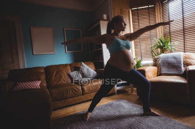 Pregnant woman performing stretching exercise in living room at home — Stock Photo