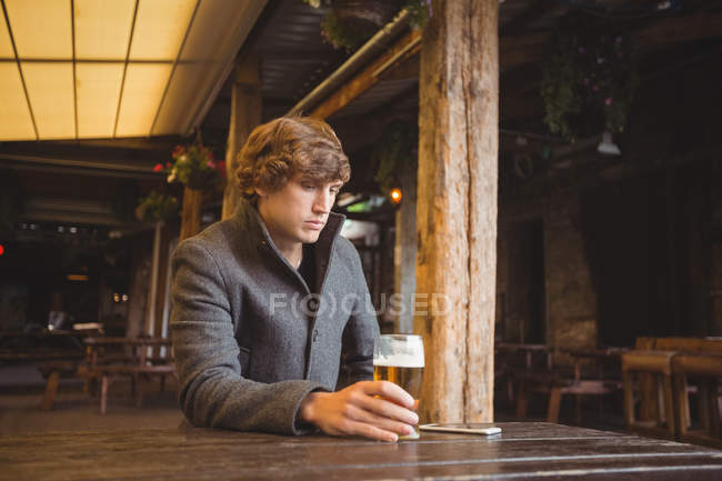Вдумчивый человек сидит в баре со стаканом пива на столе — стоковое фото