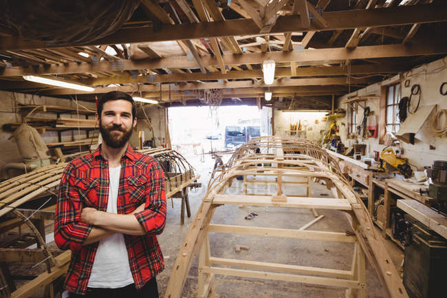 Portrait of man standing near a wooden boat frame at boatyard — Stock Photo