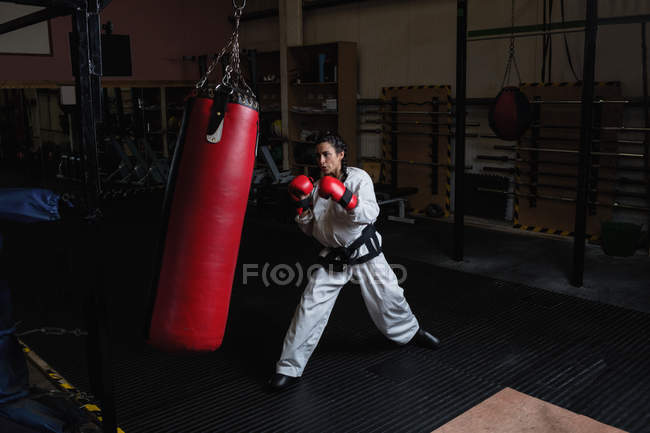 Frau im Karate-Kimono übt mit Boxsack im Fitnessstudio — Stockfoto