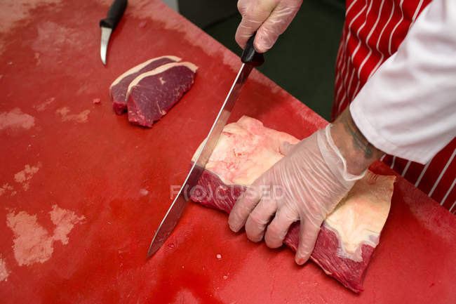 Hands of butcher slicing red meat at butchers shop — Stock Photo