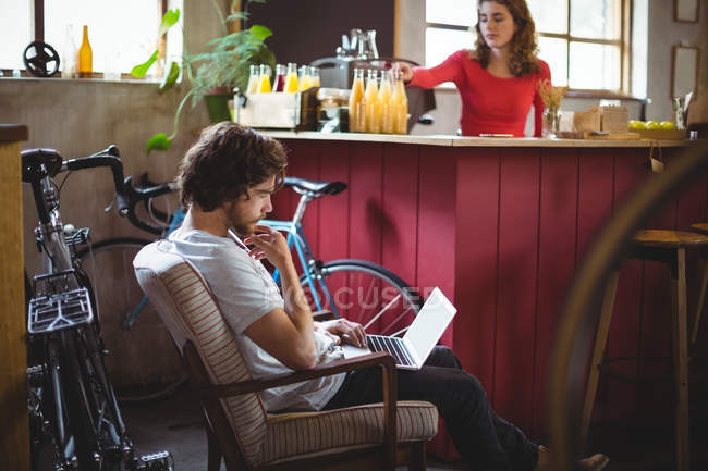 Homme assis sur une chaise et utilisant un ordinateur portable dans un magasin de vélos — Photo de stock