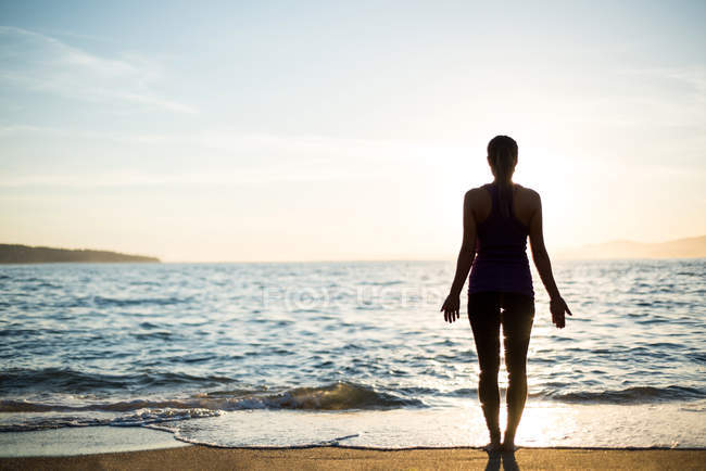 Visão traseira da mulher praticando ioga na praia no dia ensolarado — Fotografia de Stock