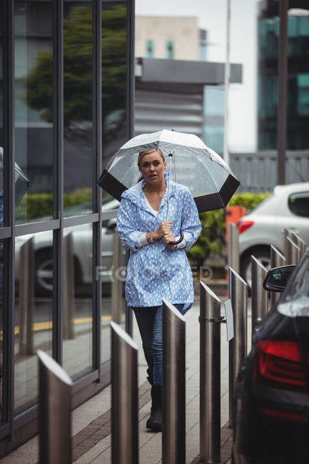 Hermosa mujer sosteniendo el paraguas y caminando en la pasarela durante el tiempo lluvioso - foto de stock