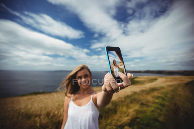 Усміхнена жінка бере селфі зі смартфоном у полі — стокове фото