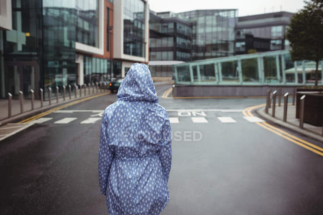 Vue arrière de la femme debout dans la rue par temps pluvieux — Photo de stock