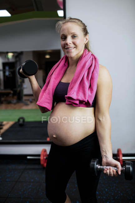 Портрет беременной женщины, поднимающей гантели в спортзале — стоковое фото
