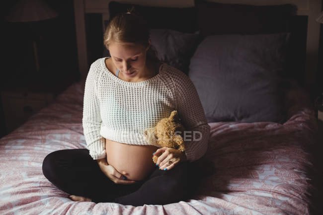 Беременная женщина держит плюшевого мишку в спальне дома — стоковое фото