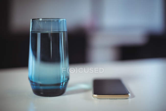 Verre d'eau et téléphone portable sur la table dans le bureau — Photo de stock