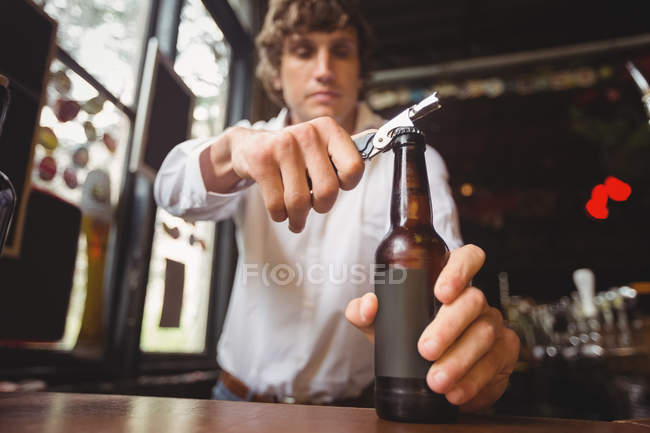 Barman abre uma garrafa de cerveja no balcão do bar — Fotografia de Stock