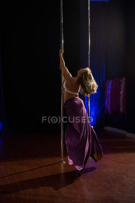 Vue arrière du danseur de pôle pratiquant la pole dance en studio — Photo de stock