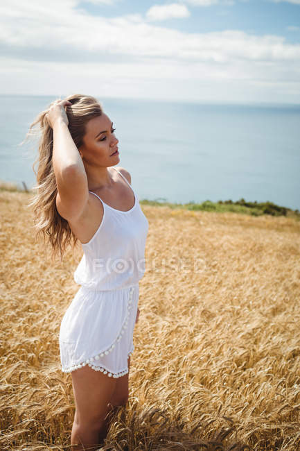 Mujer con la mano en el pelo de pie en el campo de trigo en el día soleado - foto de stock