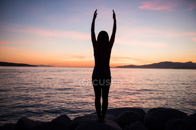 Visão traseira da mulher realizando ioga na rocha ao entardecer — Fotografia de Stock